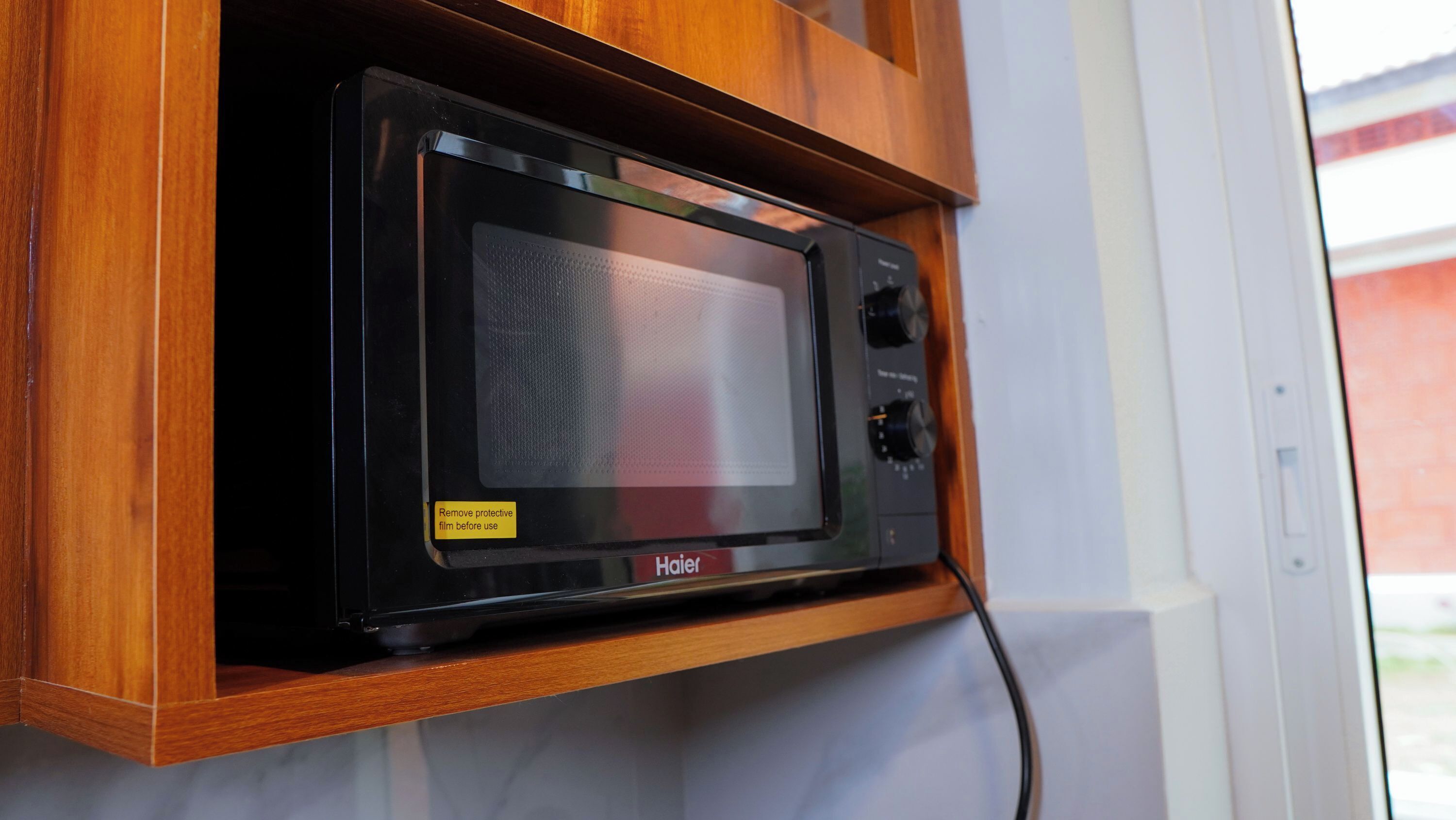 Um forno de micro-ondas Haier preto fixado numa prateleira de madeira.
