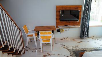 Una habitación con un mueble bajo de madera para el televisor, una silla blanca con cojines amarillos, piso de mármol y una escalera.