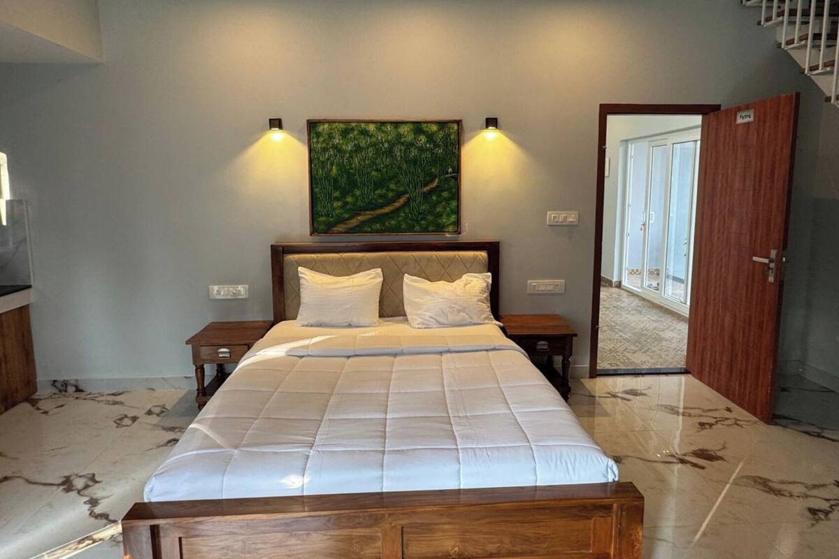 A bedroom with a bed, two bedside tables, a painting on the wall, and a door leading to another room.