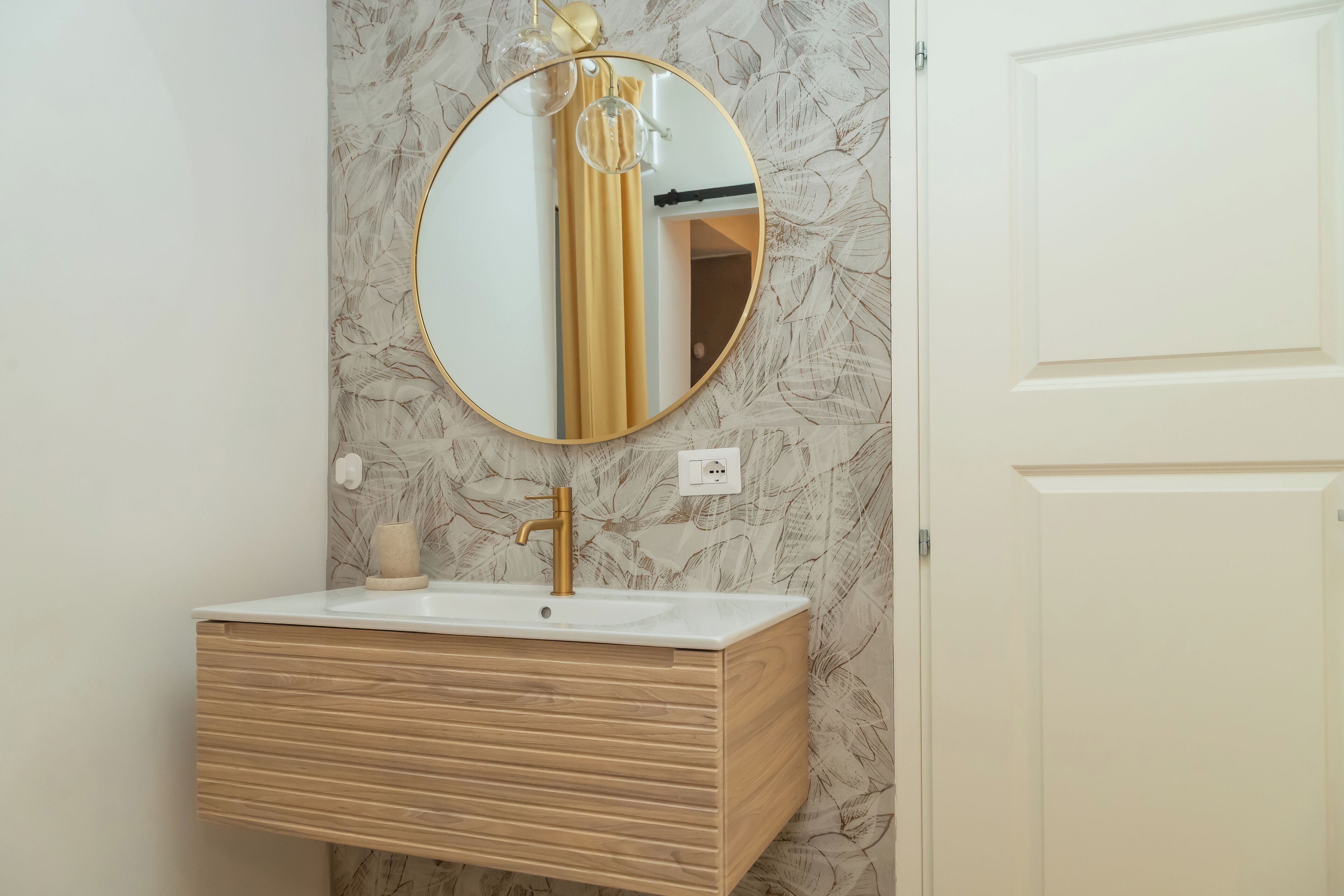 A bathroom with a wooden vanity, a gold faucet, and a round mirror.
