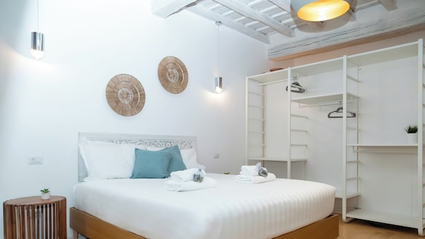 A neatly arranged bedroom with a wooden bed, white bedding, a small round side table, and a white wardrobe with shelves.