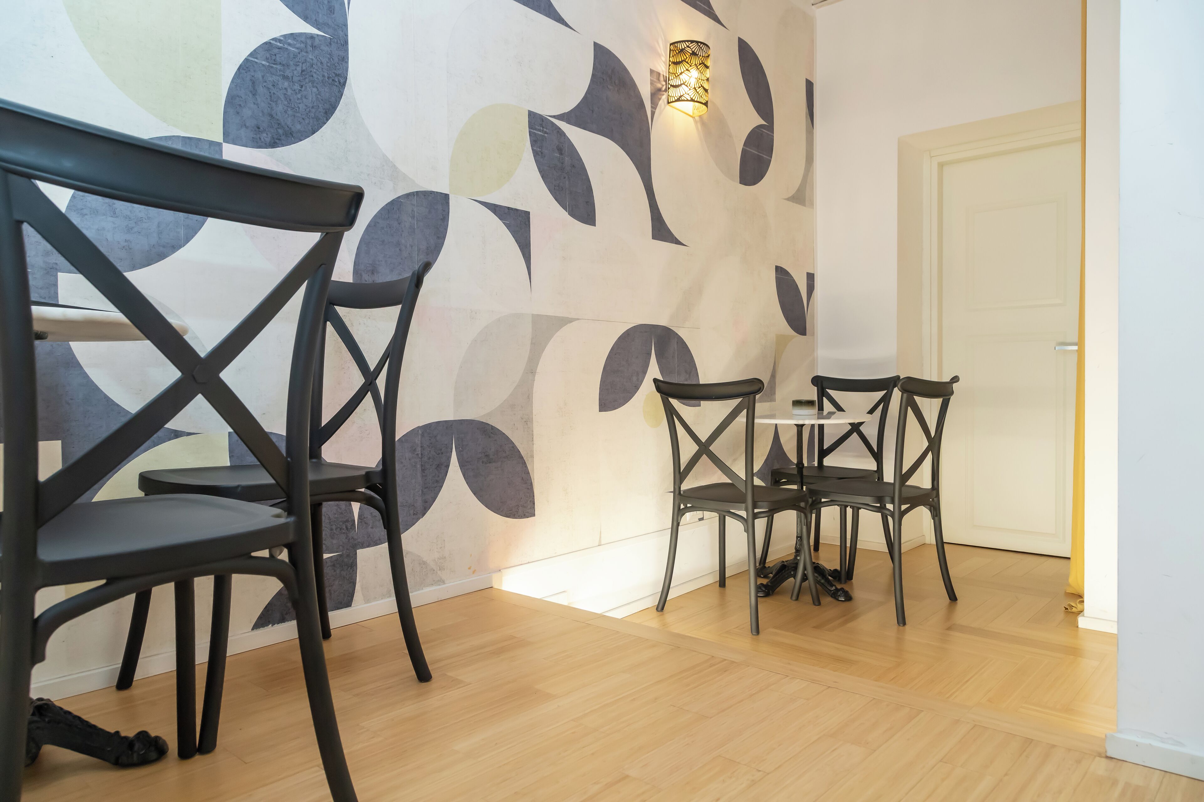 Un espace repas avec des chaises et une table au design moderne, un mur orné d’un motif et une porte.