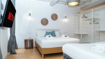 Una habitación de hotel moderna con una cama, una pantalla de televisión mostrando 'NETFLIX', un armario y una pequeña mesa redonda con una planta.
