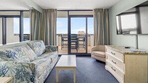 A hotel room with a sofa, a small table, a dresser, a TV, and a balcony with a table and chairs. - Salt life made Simple at Grande Shores (Myrtle Beach)