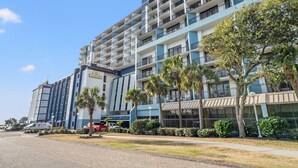 A multi-story hotel with balconies, palm trees, and a clear sky. - Salt life made Simple at Grande Shores (Myrtle Beach)