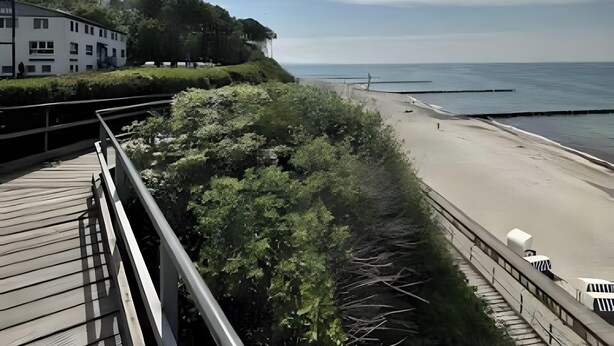 A coastal view with a beach, a wooden deck, and a building with a white facade.