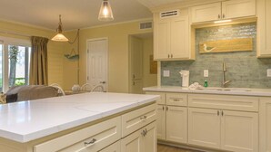 A kitchen with white cabinets, a large island, pendant lighting, and a backsplash. - Renovated Ground-floor Condo W/ Heated Pools 1 Bedroom Condo (South Padre Island)