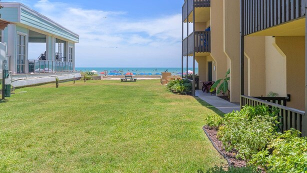 A hotel courtyard with a grassy lawn, outdoor seating, and a view of the beach. - Renovated Ground-floor Condo W/ Heated Pools 1 Bedroom Condo (South Padre Island)