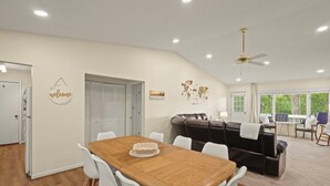 Uma sala de estar espaçosa com uma mesa de jantar de madeira, cadeiras brancas, um sofá de couro preto e um ventilador de teto.