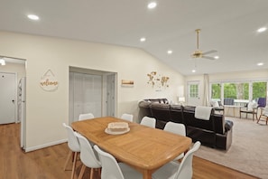 A spacious living area with a wooden dining table, white chairs, a black leather sofa, and a ceiling fan. - Sunset Retreat! Level Entry! 3BR! Park & Trails (Beech Mountain)