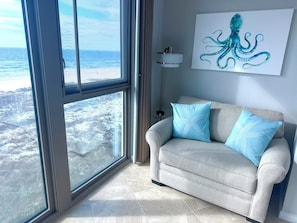 A room with a large window overlooking a snowy landscape, a grey sofa with blue pillows, and a wall-mounted painting of an octopus. - Escape to Salty~Kisses • Gorgeous beachfront views + Boating at Perdido Towers (Pensacola)