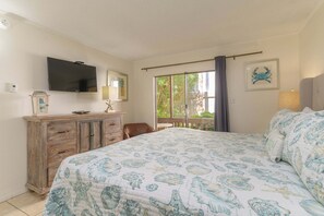 A bedroom with a bed, a TV, a dresser, and a balcony with a view of greenery. - Tiki 112 - Beachfront 1br Condo W/ Pool Access 1 Bedroom Condo (South Padre Island)