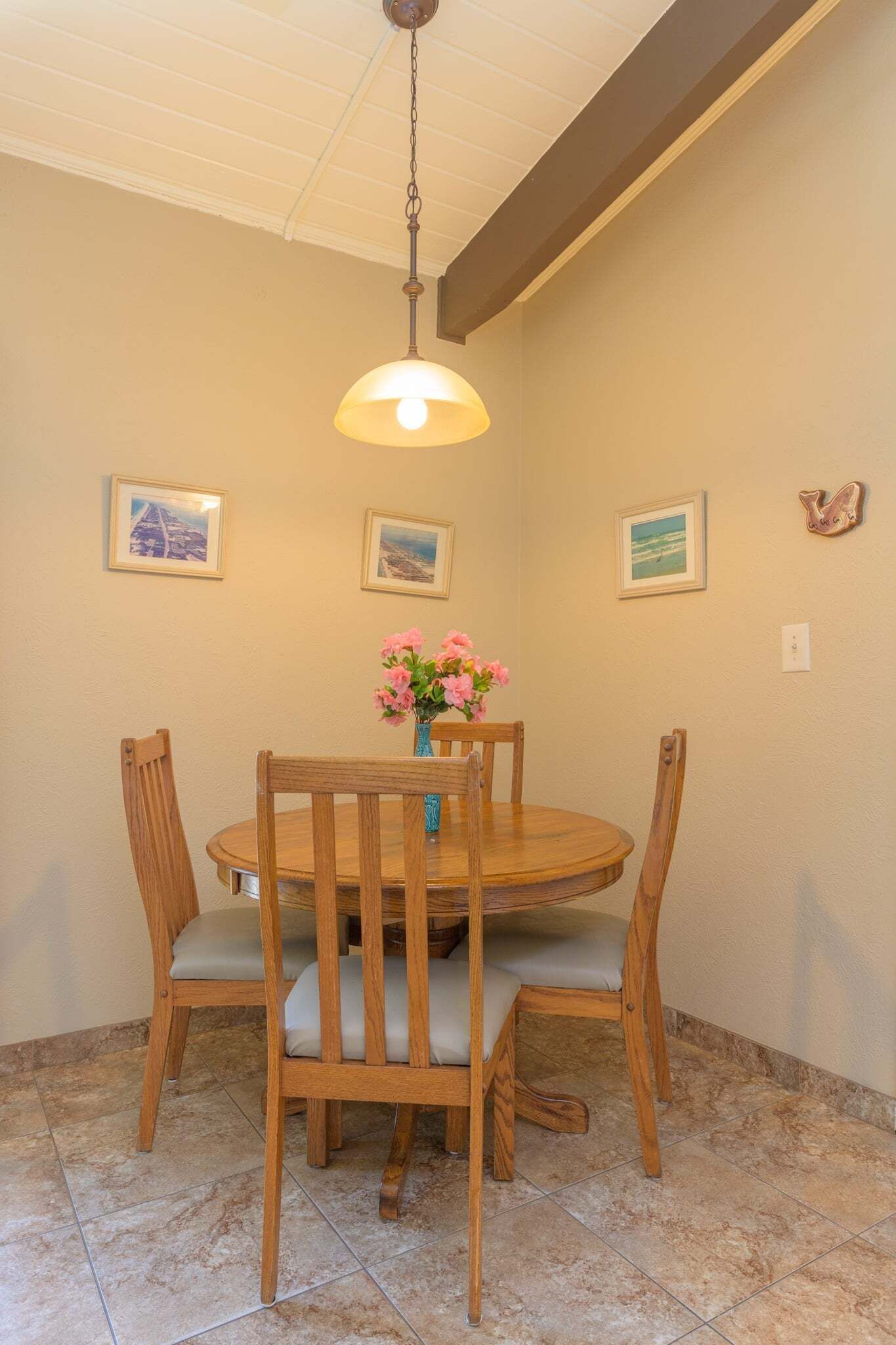 Un'area pranzo con un tavolo e sedie in legno, una lampada a sospensione e quadri appesi al muro.