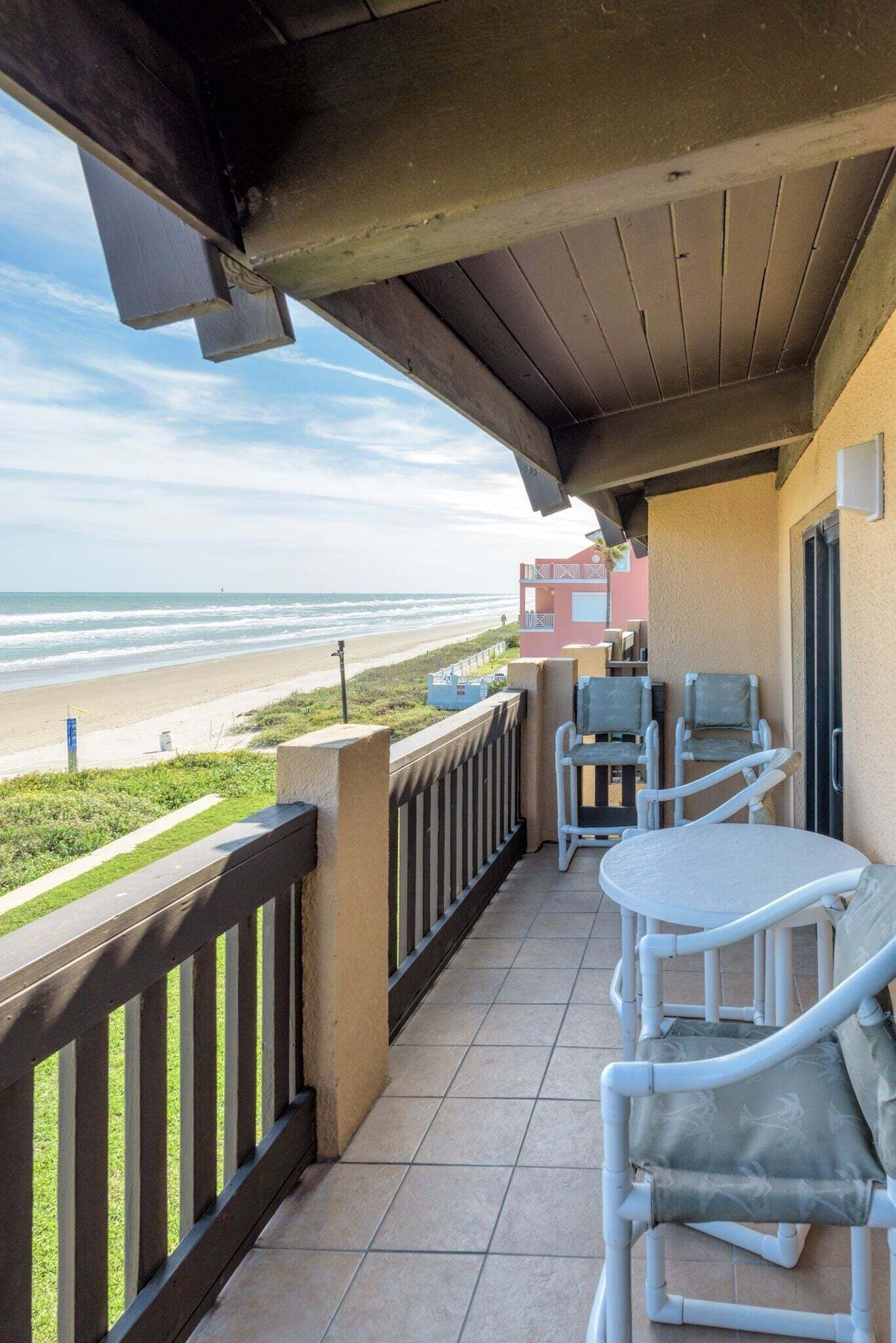 A balcony with a view of the beach, two white wicker chairs, and a small table.