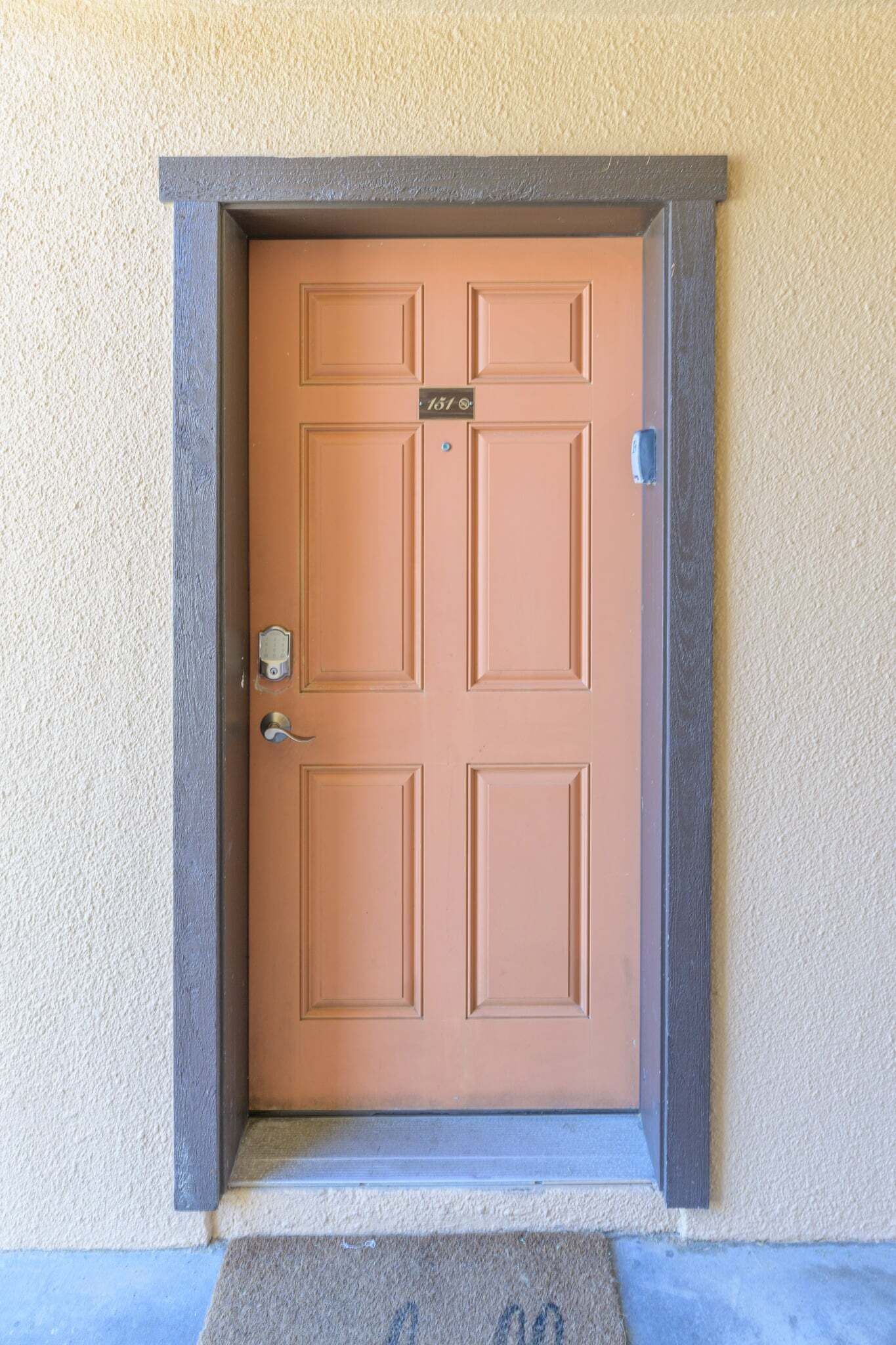 A brown door with a number plate, a doorbell, and a mail slot.
