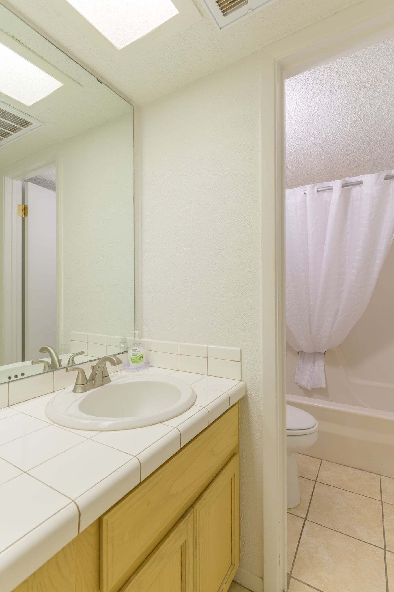 Un baño con lavamanos, espejo e inodoro blancos.