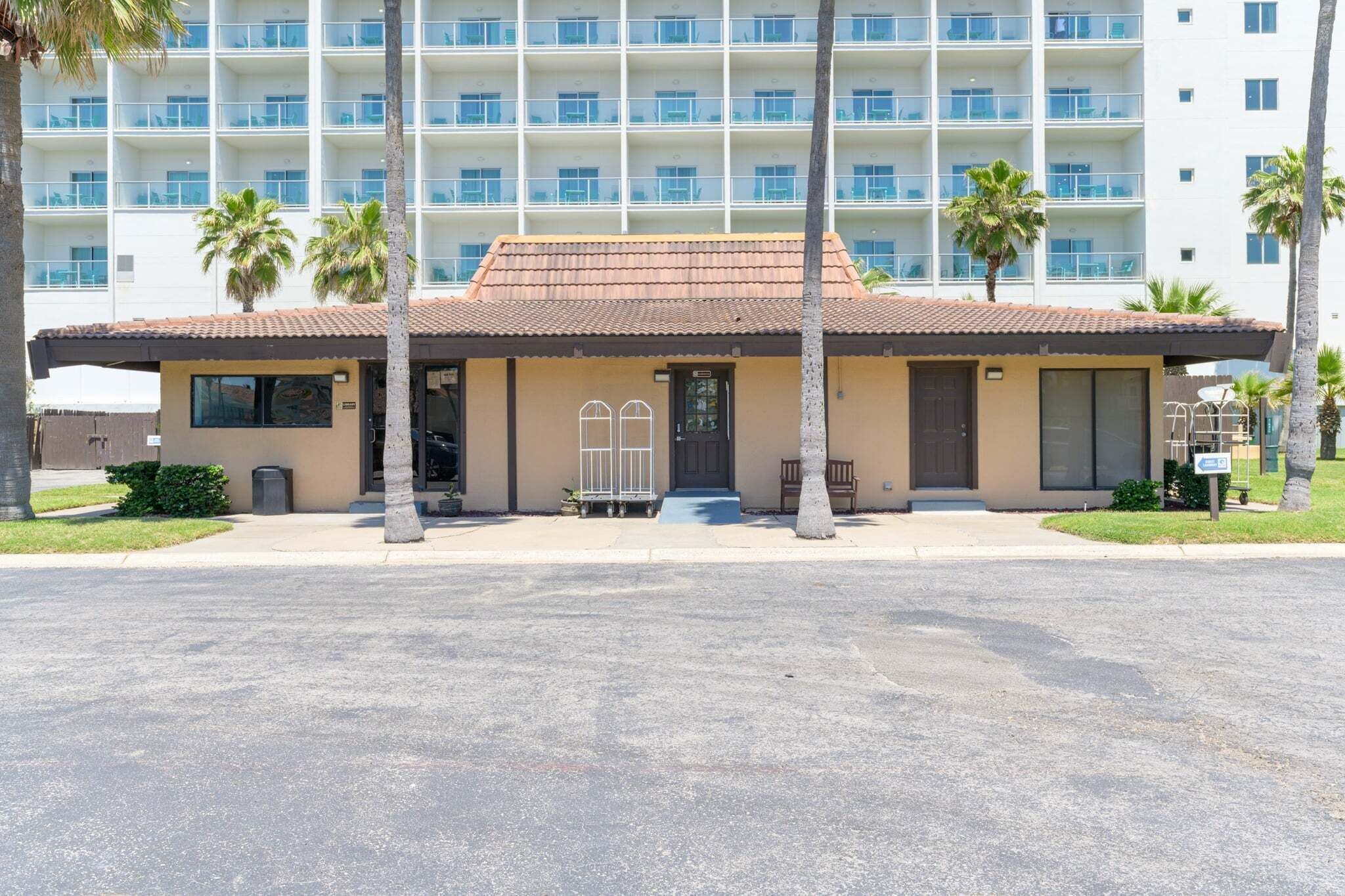 A hotel with a flat roof, multiple floors, and a parking lot in front.