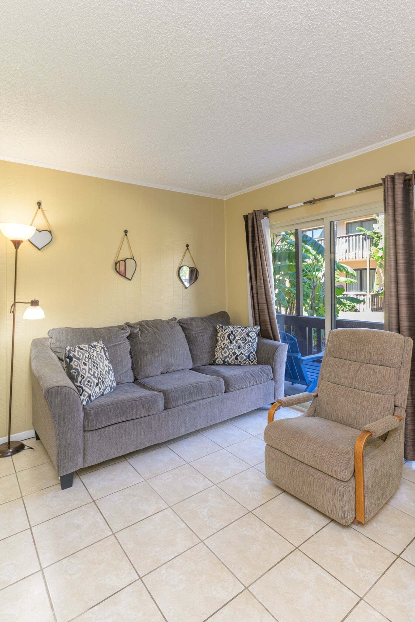A living room with a grey sofa, a patterned throw pillow, a wooden armchair, and a floor lamp.