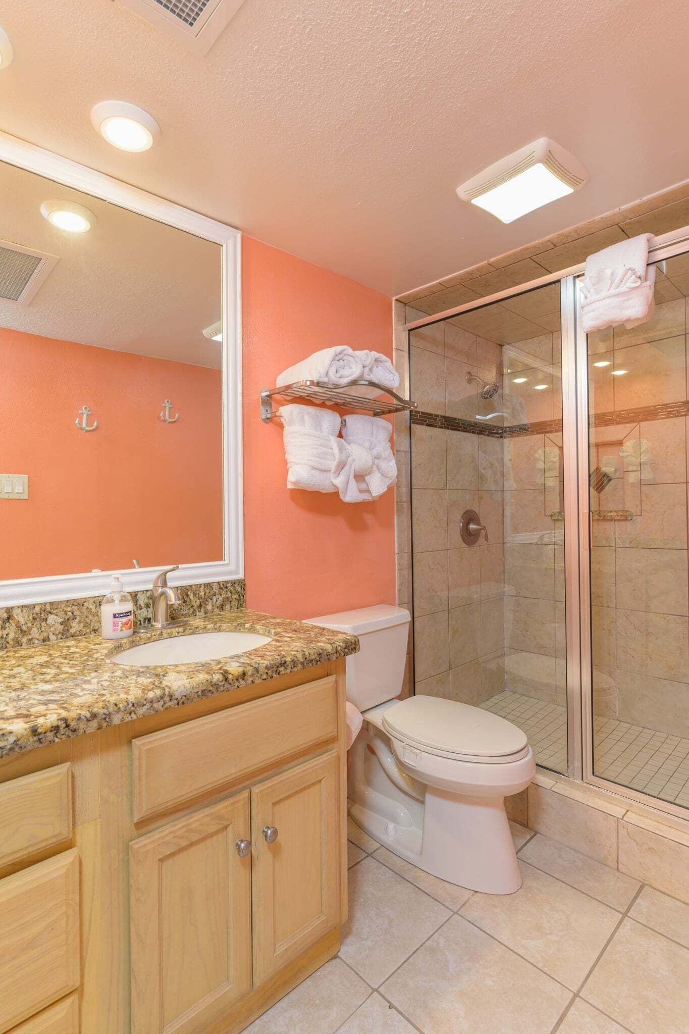 Une salle de bain dotée d’un comptoir en granit, de toilettes blanches, d’une douche en verre et d’un grand miroir.