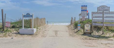 A beach entrance with signs indicating beach access, no motor vehicle parking, and overnight camping is prohibited.