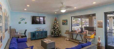 A cozy lounge area with wicker furniture, a Christmas tree, and a TV mounted on the wall.