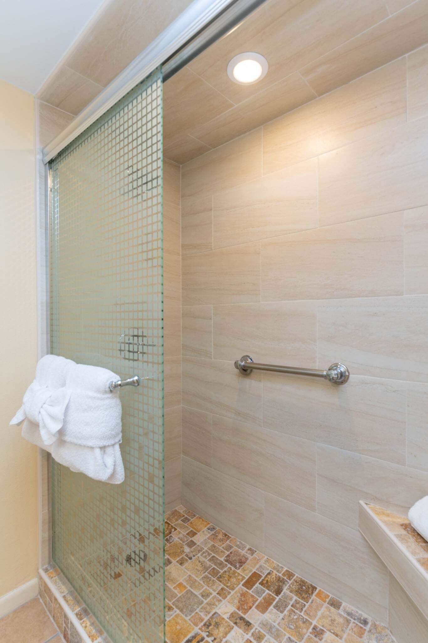 A shower with a glass door, a towel rack, and a handrail.