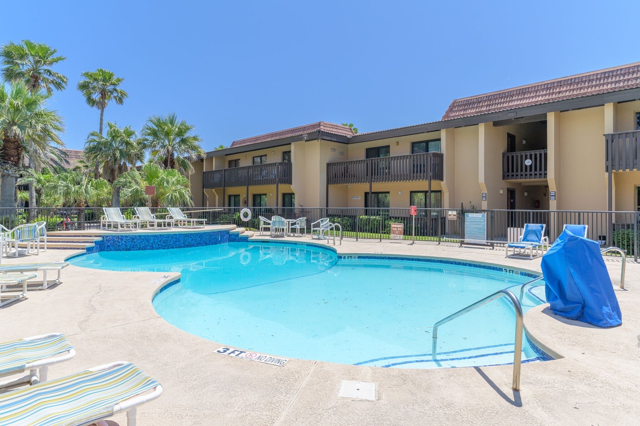A swimming pool with lounge chairs, a small hot tub, and a building with balconies.