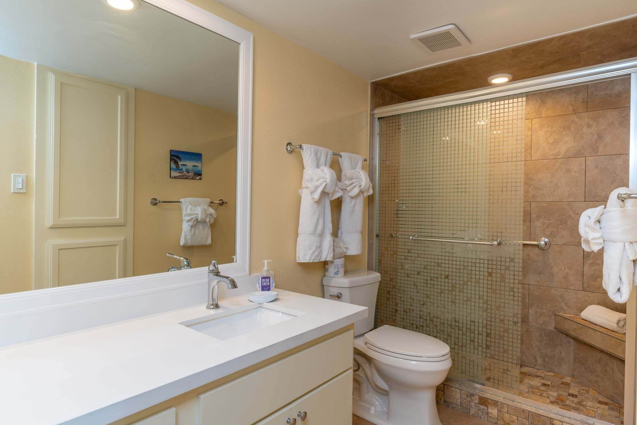 A bathroom with a white sink, mirror, and toilet, a glass shower enclosure, and towels hanging on a rack.