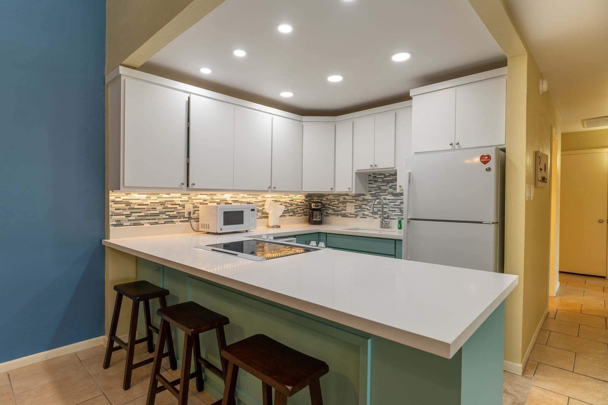Una cocina moderna con armarios blancos, una isla grande con taburetes, un microondas y un refrigerador.