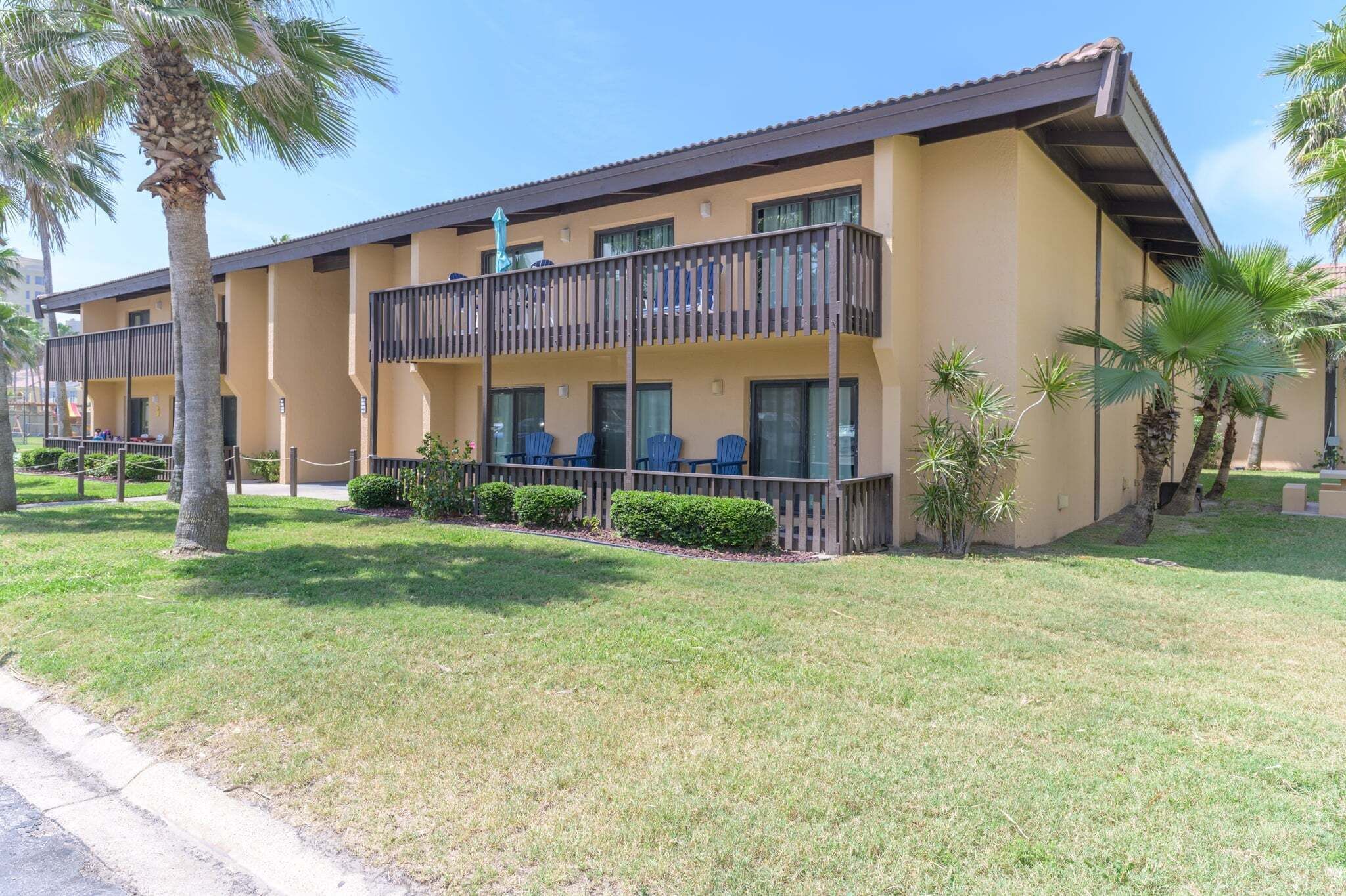 A two-story motel with a balcony on the second floor, surrounded by palm trees and a well-maintained lawn.