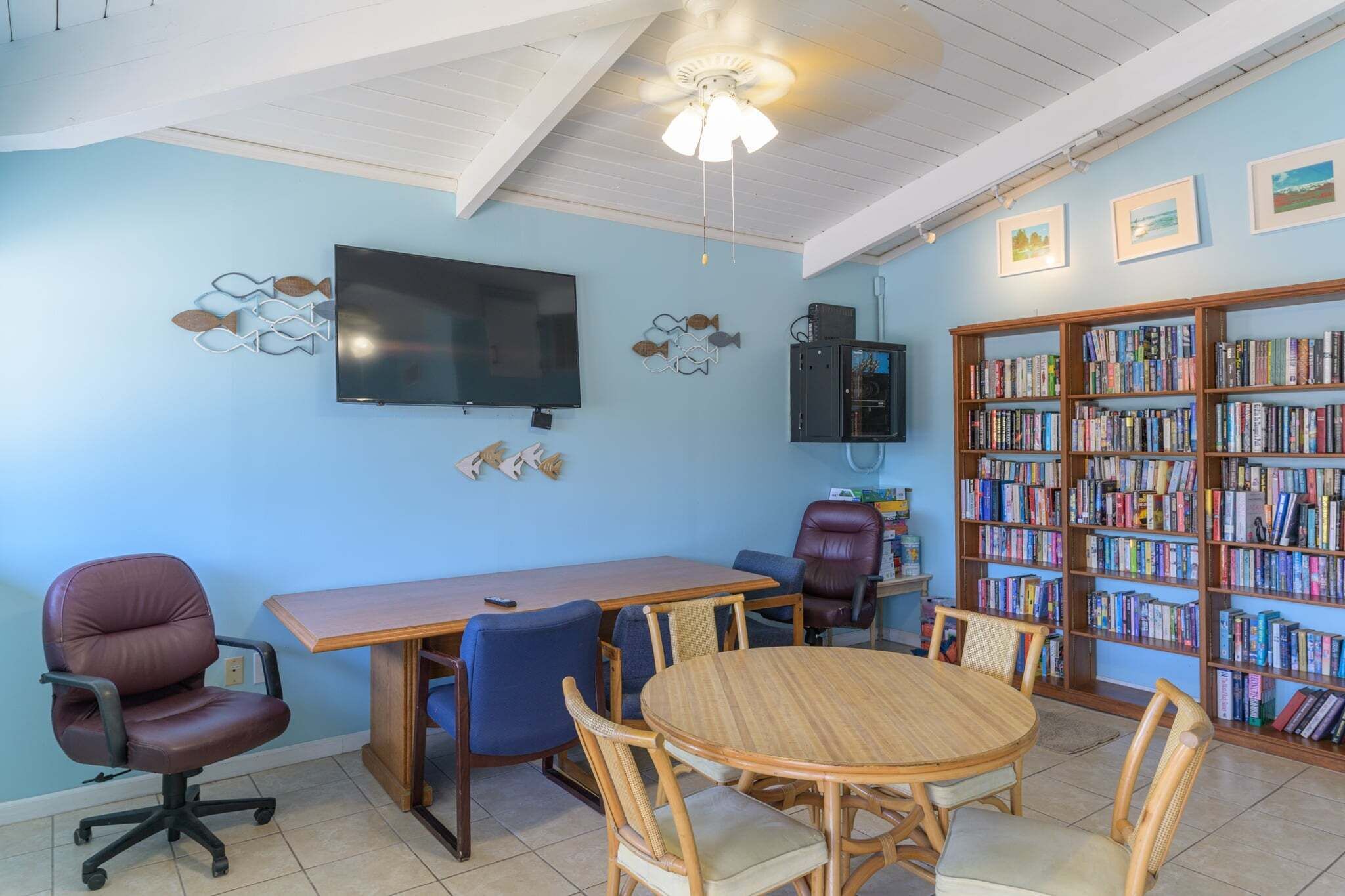 Una habitación con una mesa de madera, sillas, un televisor, una estantería y un ventilador de techo.