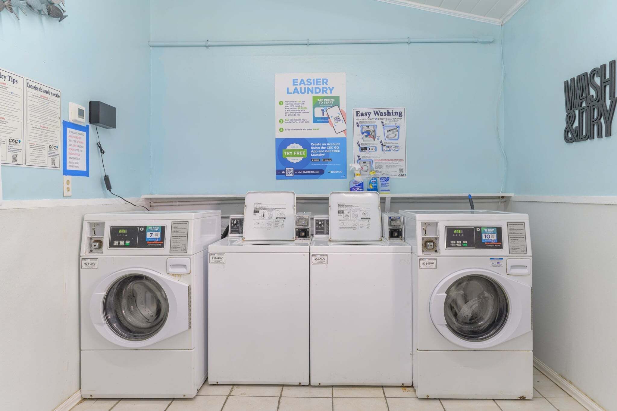 A laundry area with three washing machines, a poster on the wall, and a sign for 'WASH & DRY'.