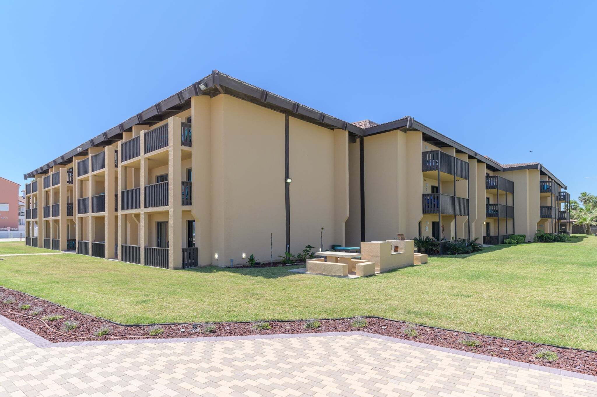 A multi-story hotel with a flat roof, balconies, and a paved courtyard.
