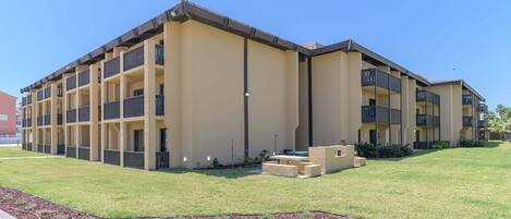 A multi-story hotel with a flat roof, balconies, and a paved courtyard.