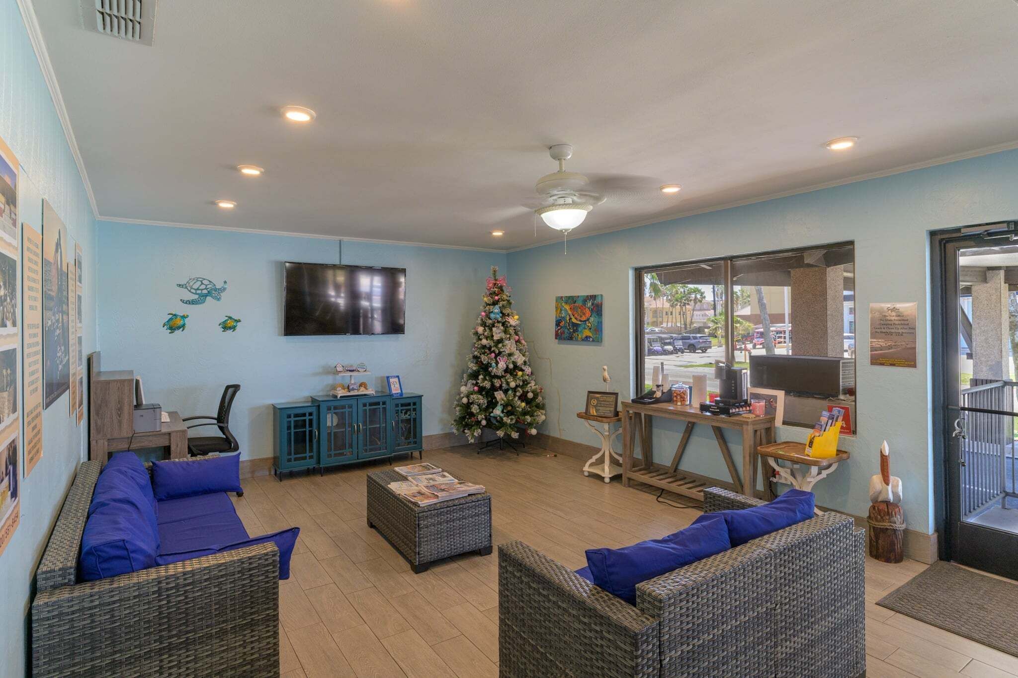 A cozy lounge area with wicker furniture, a Christmas tree, and a TV mounted on the wall.