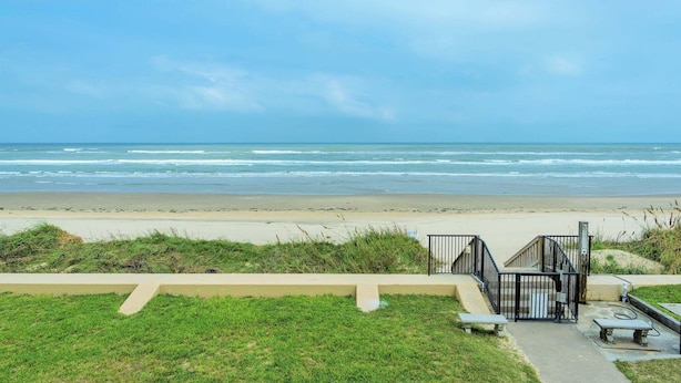 Vista de una playa con un paseo de concreto, escalones y una barandilla de metal que dan acceso a la playa.