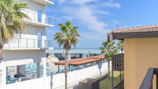 A hotel with a pool area, palm trees, and a view of the ocean. - Tiki 318 - Lovely One Bedroom Beachfront Property 1 Condo (South Padre Island)