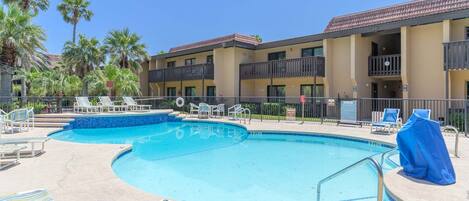 A pool area with lounge chairs and a building with balconies.