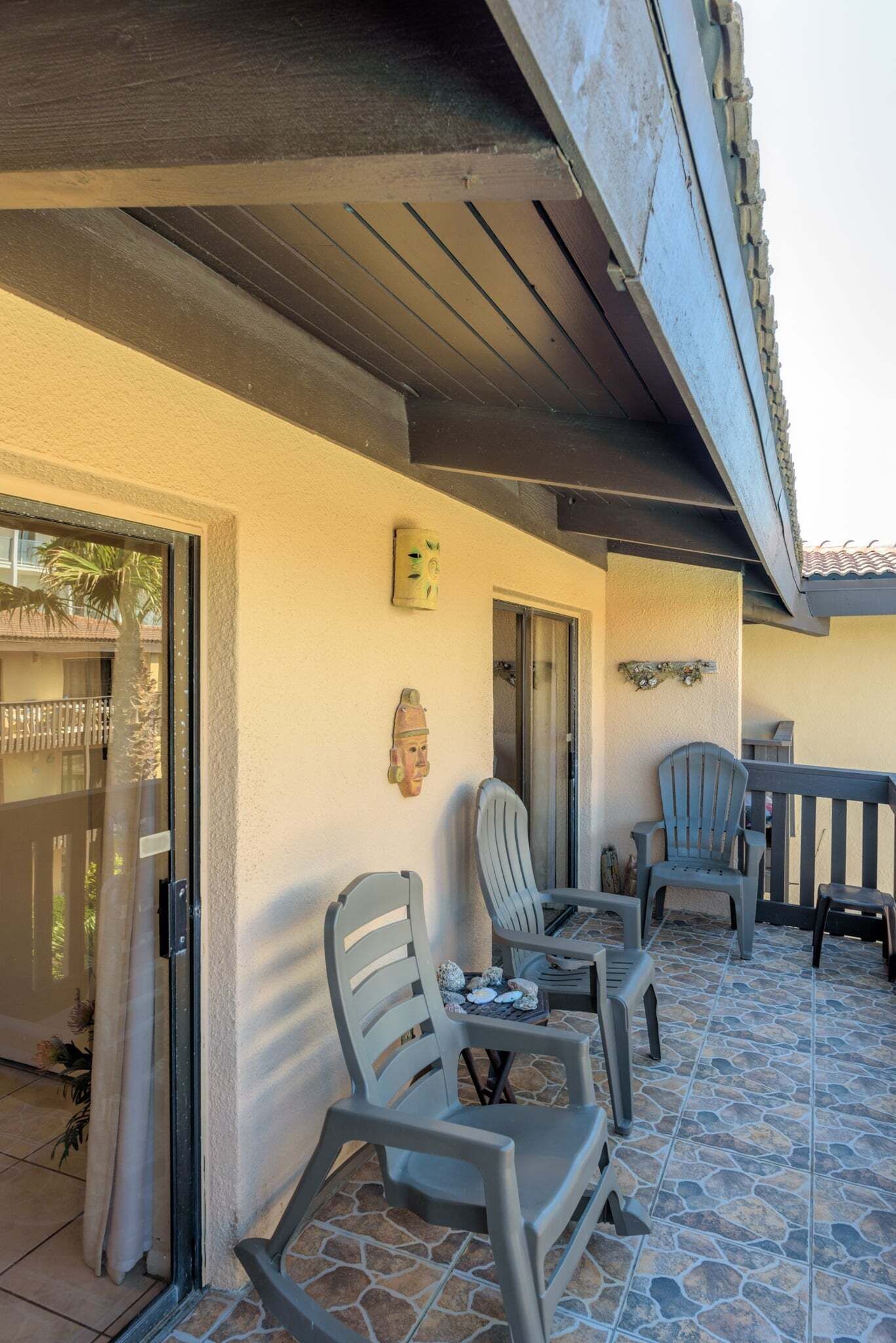 An outdoor patio area with stone flooring, a covered seating area with chairs and tables, and a door leading to a covered entrance.
