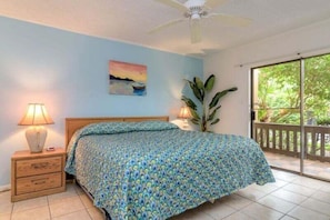 A bedroom with a bed, nightstands, a ceiling fan, a painting, and a view through a window. - Tiki 111 - Ocean View Condo In South Padre Island 1 Bedroom Condo (South Padre Island)