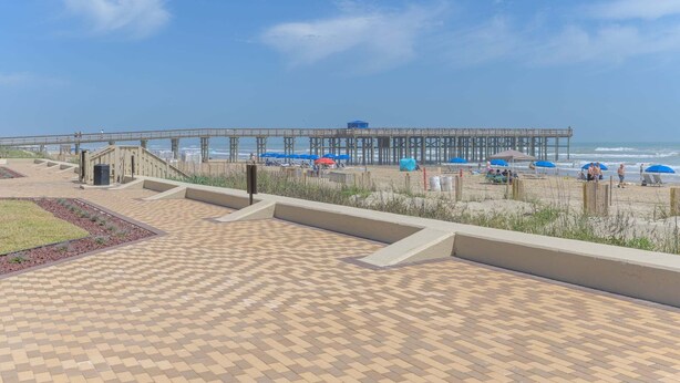 Eine Uferpromenade mit einem Steg, der sich ins Meer erstreckt, mit überdachter Sitzgelegenheit und einer Treppe zum Strand.
