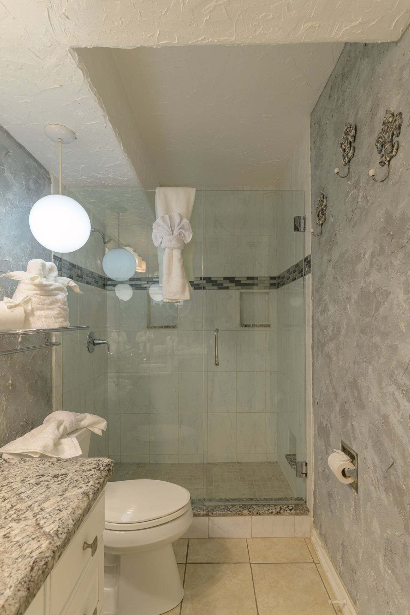 Une salle de bain dotée d’une douche à parois de verre, de toilettes et d’un meuble-lavabo avec un plan de travail en marbre.