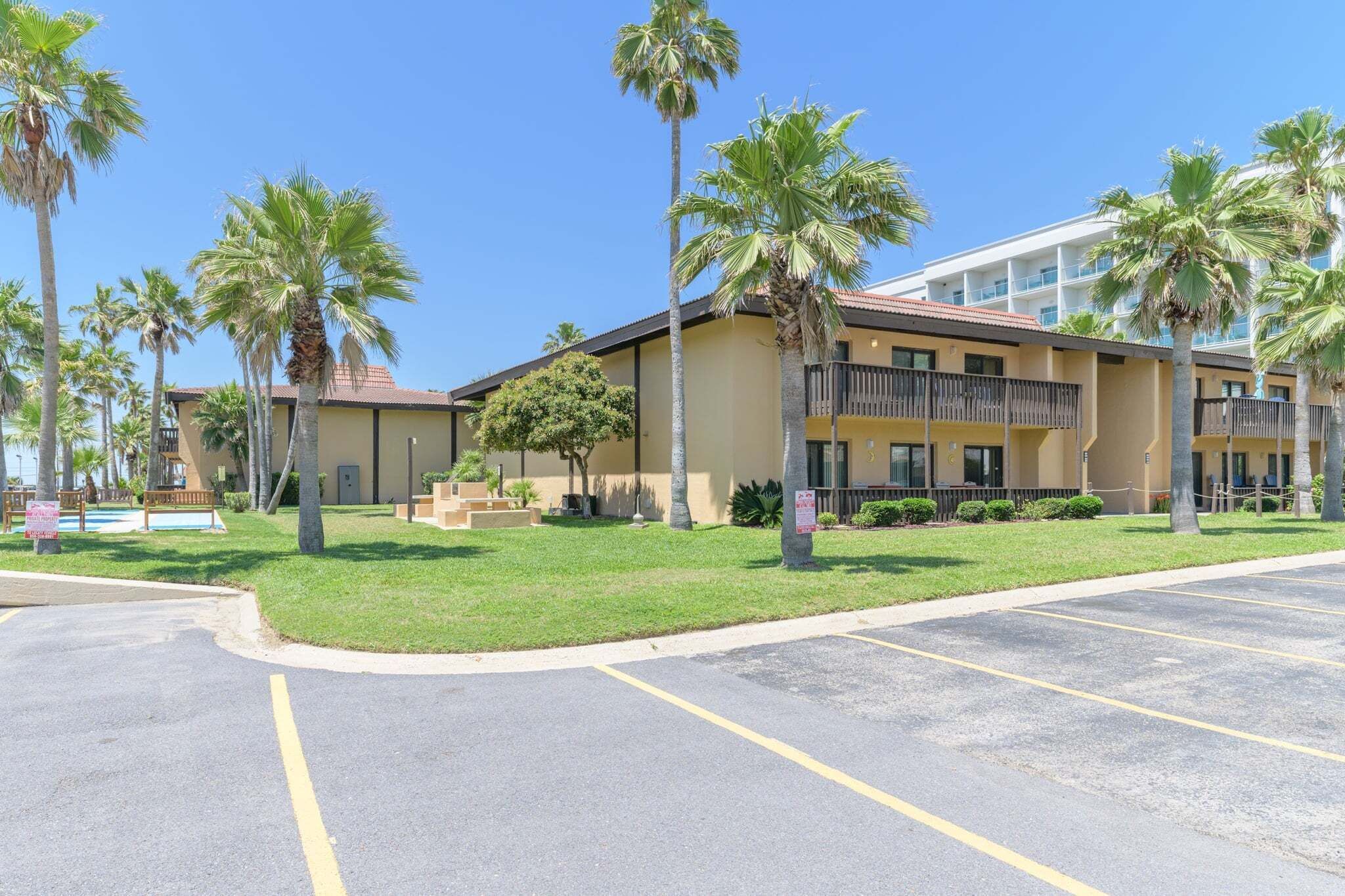 Un hotel con fachada amarilla, palmeras y estacionamiento.