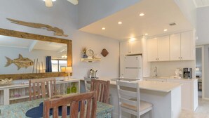 Una cocina moderna con armarios blancos, una isla central y un comedor con sillas y una mesa de madera.