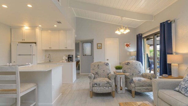 Una cocina moderna con armarios blancos, un comedor con mesa y sillas de madera, y una sala de estar con sofá y sillones.