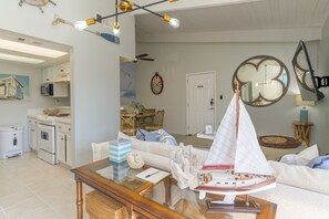Eine moderne Küche mit weißen Geräten, ein Essbereich mit Holztisch und -stühlen sowie ein Wohnzimmer mit einem Modell eines Segelbootes.