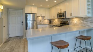 A modern kitchen with white cabinets, stainless steel appliances, and a large island with bar stools. - Tiki 128 - Spacious Ocean View 1br Condo Sleeps 6 1 Bedroom Condo (South Padre Island)