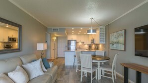 A modern kitchen with white cabinets, a central island, and a dining area with a round table and chairs. - Tiki 128 - Spacious Ocean View 1br Condo Sleeps 6 1 Bedroom Condo (South Padre Island)