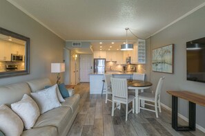 A modern kitchen with white cabinets, a central island, and a dining area with a round table and chairs. - Tiki 128 - Spacious Ocean View 1br Condo Sleeps 6 1 Bedroom Condo (South Padre Island)