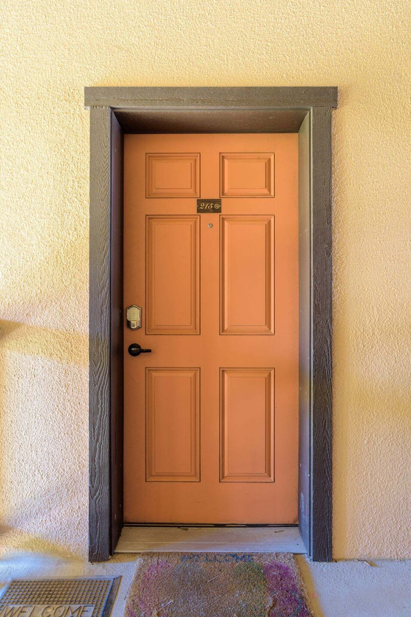 A closed wooden door with a number plate, a doorbell, and a doormat with "WELCOME" written on it.